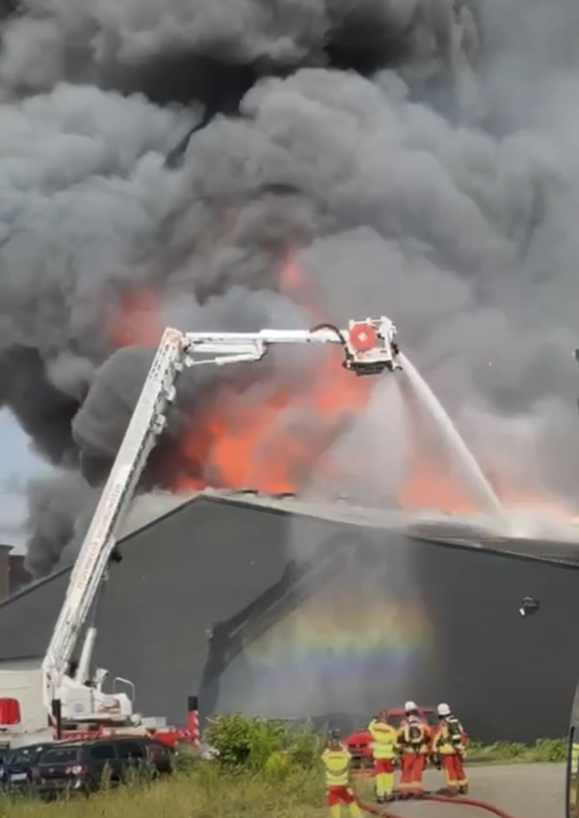 Lagerhalle in Vollbrand, davor ein Teleskopmast der Feuerwehr.